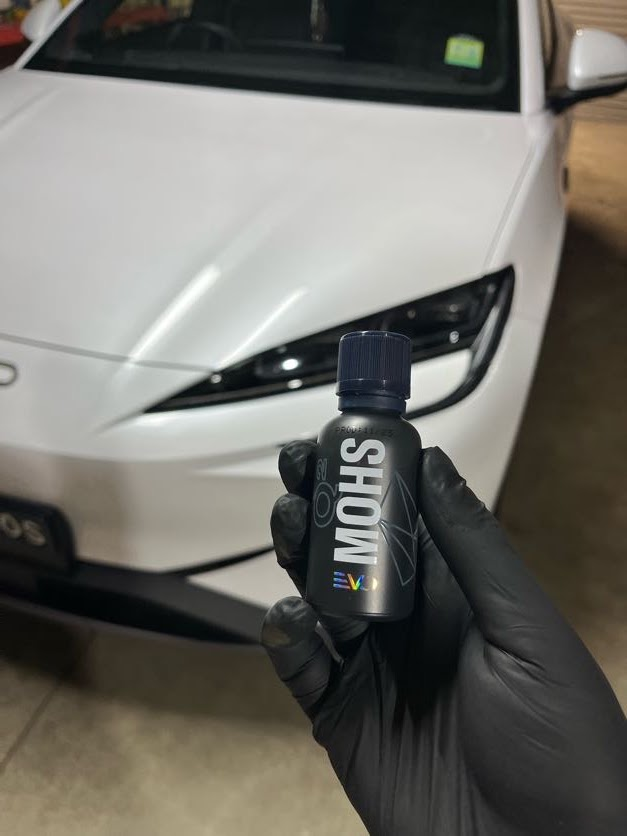 MOHS ceramic coating bottle held in front of a freshly detailed white sedan